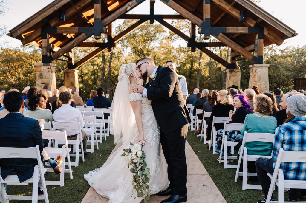 bride and groom kissing during the recessional of their sunset wedding ceremony at the springs venue in denton, texas