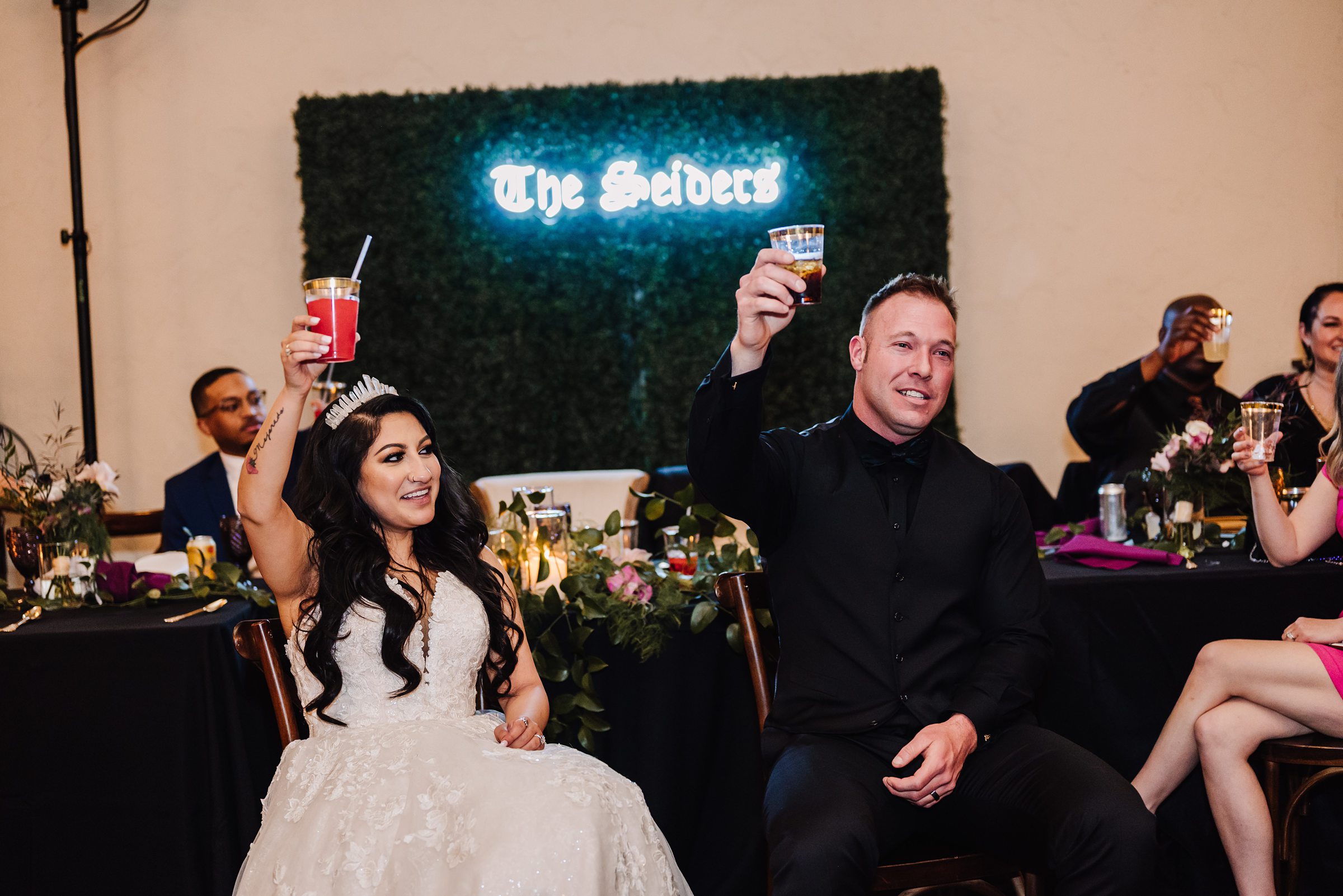 bride and groom toasting with custom neon sign backdrop